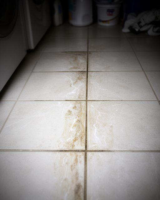 Laundry room tile with detergent residue and dingy grout before professional washing